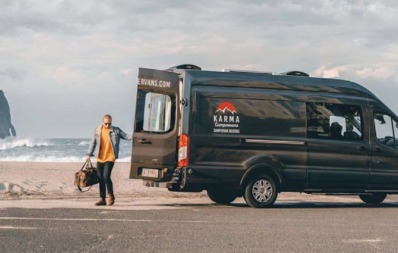 A Karma campervan parked by the ocean with a man standing behind it.