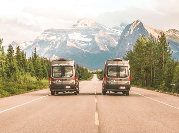 Two Karma campervans driving with the Canadian Rockies in the distance.