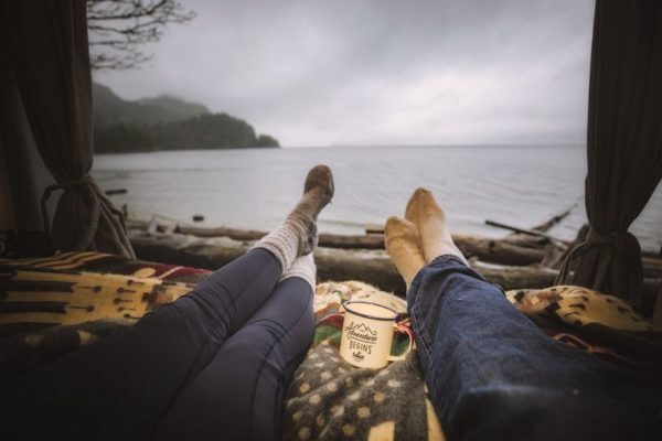 Two people lying down looking at the view of the ocean from their campervan.