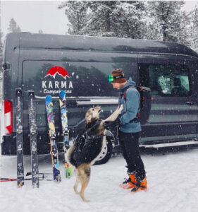 a man and a dog are standing in the snow by a camper van