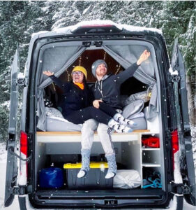 a man and woman are sitting in the back of a camper van during the winter