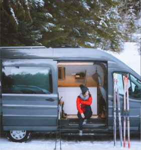 a woman sitting inside a camper van with her skis