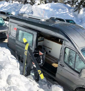 a man in a ski suit is standing in the snow by a camper van