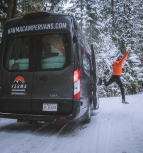 a person is jumping in snow near camper van