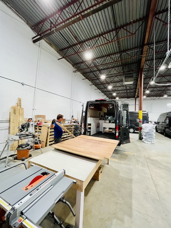 A custom campervan is in the process of being built inside a workshop.