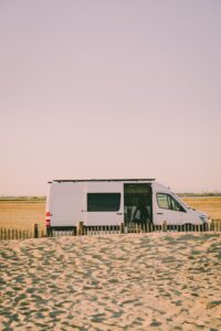 a campervan van parked in a sandy area next to a beach