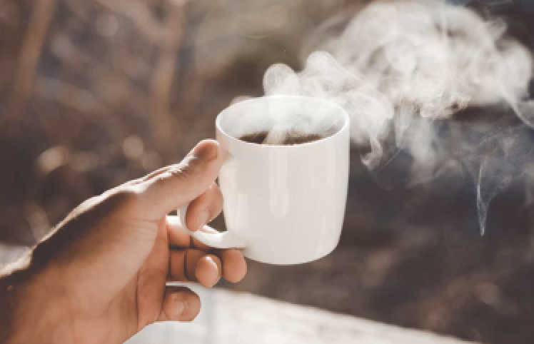 A hand holding a steaming cup of coffee.