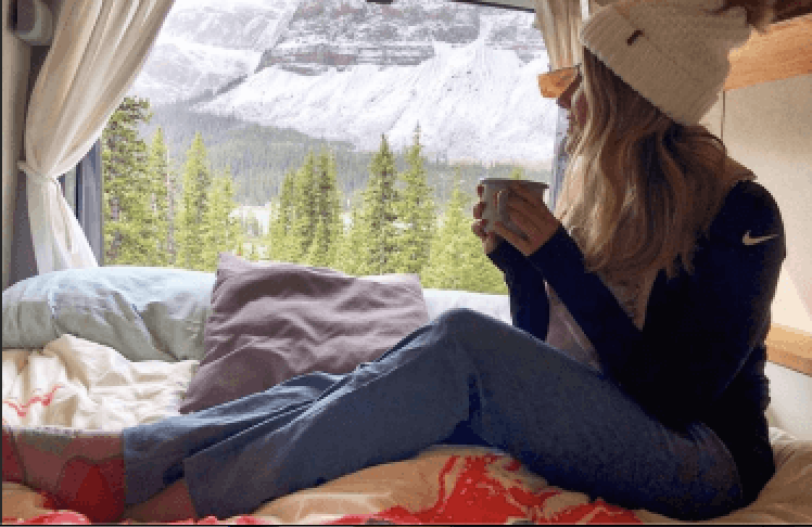 A woman sitting inside a campervan with a cup of coffee.